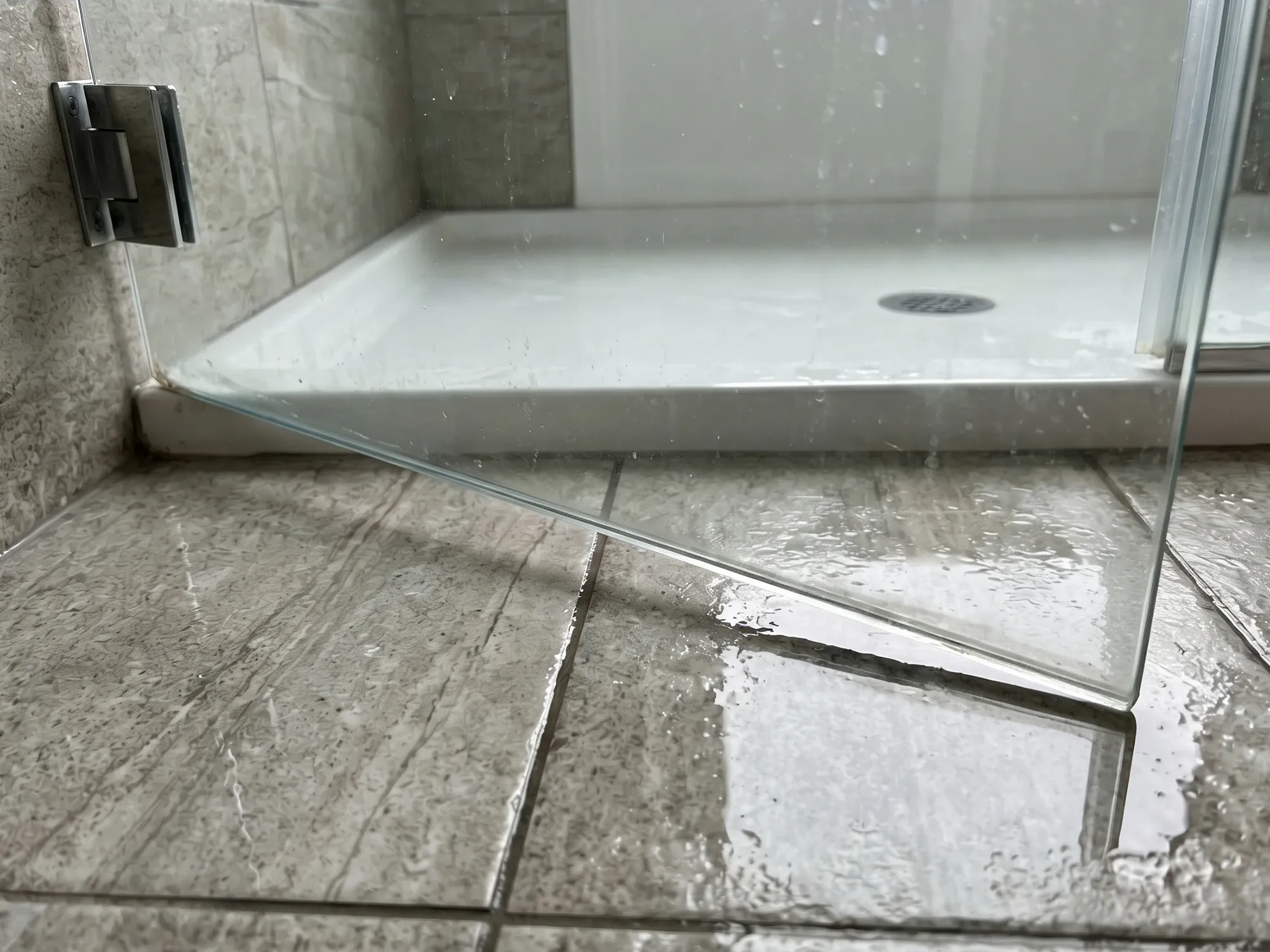 Sagging frameless shower door panel sitting lower than at install, a sign of worn hinges