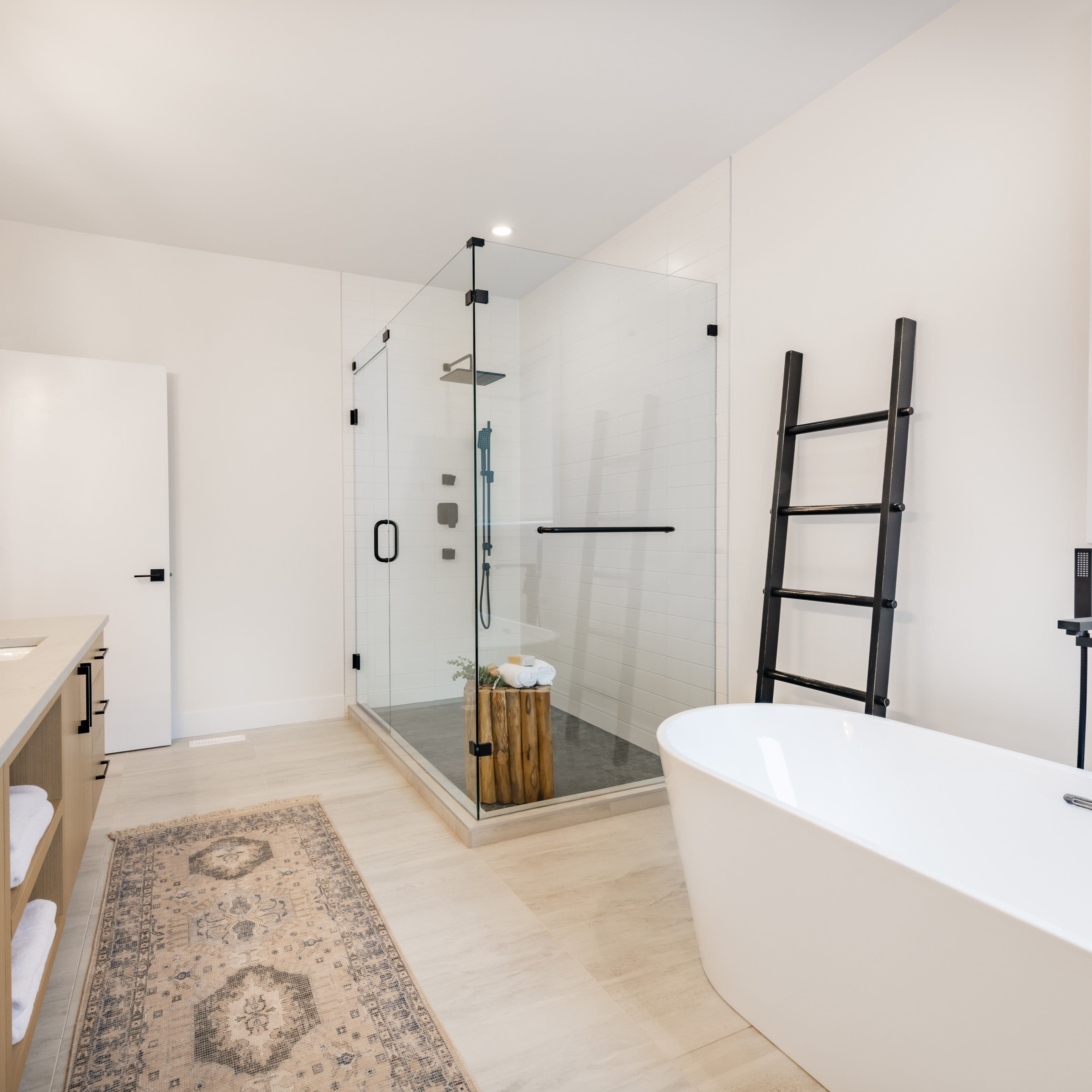 Spacious bathroom with a frameless glass walk-in shower, freestanding bathtub, and a chic wooden stool accent for a luxurious spa-like ambiance.