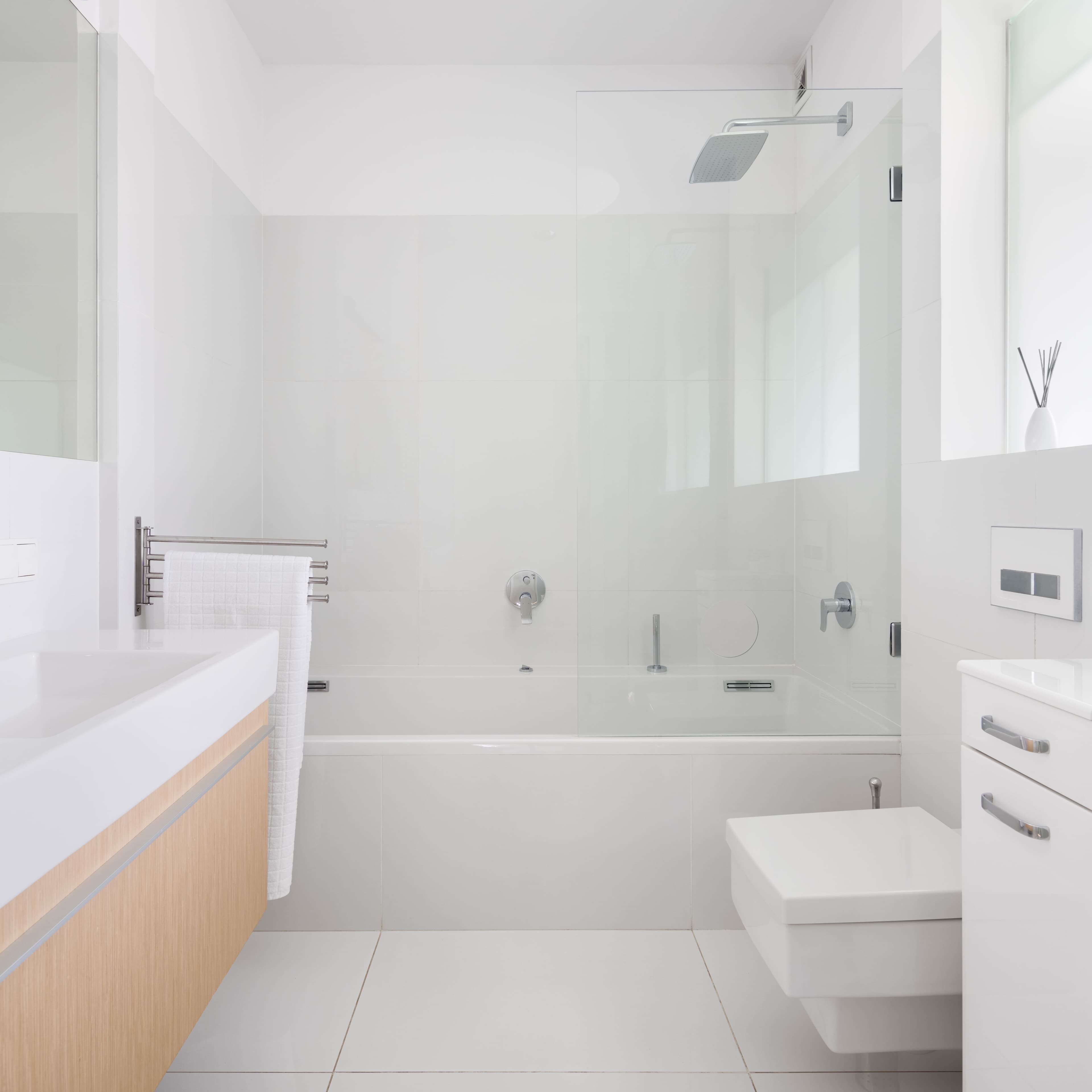 Modern bathroom with a frameless glass shower enclosure, floating vanity, and sleek fixtures, designed in a minimalistic all-white theme.