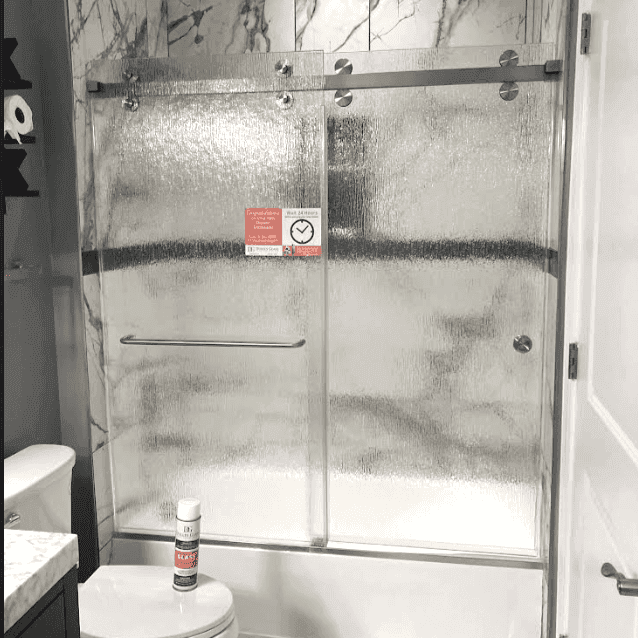 Modern bathroom with frosted glass sliding shower doors, textured finish for privacy, and elegant marble tile wall accents.