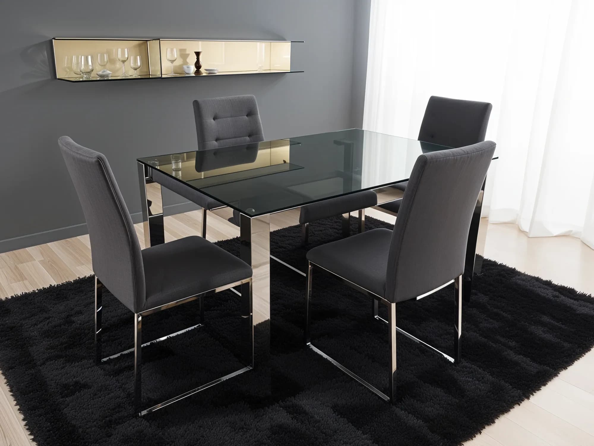 A chic modern dining room featuring a rectangular table with a tinted grey glass top and a reflective chrome base, complemented by four grey upholstered chairs on a black shag rug.