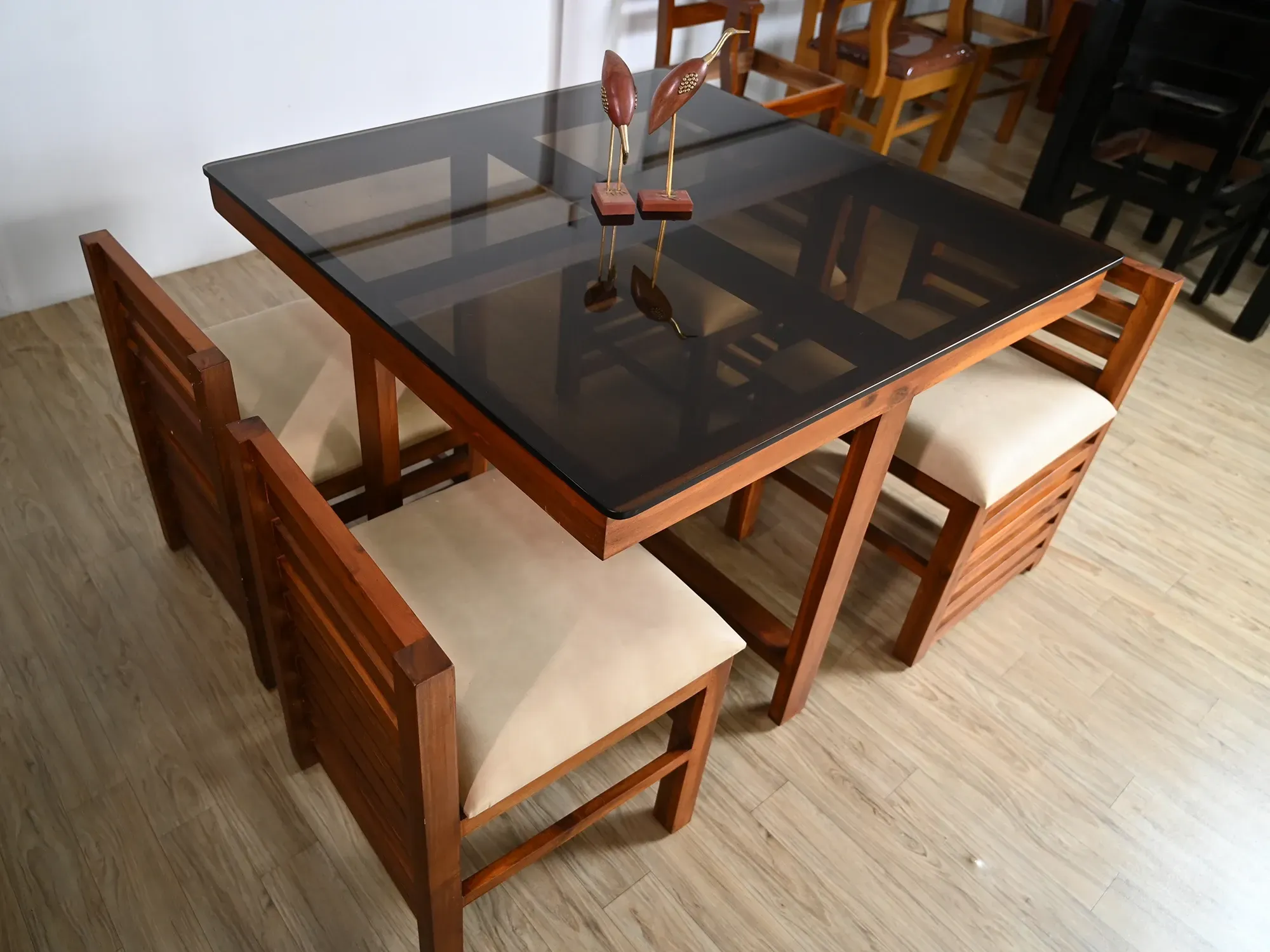 A wooden dining set for four, featuring a square table with a dark, tinted bronze glass top for a contemporary look.