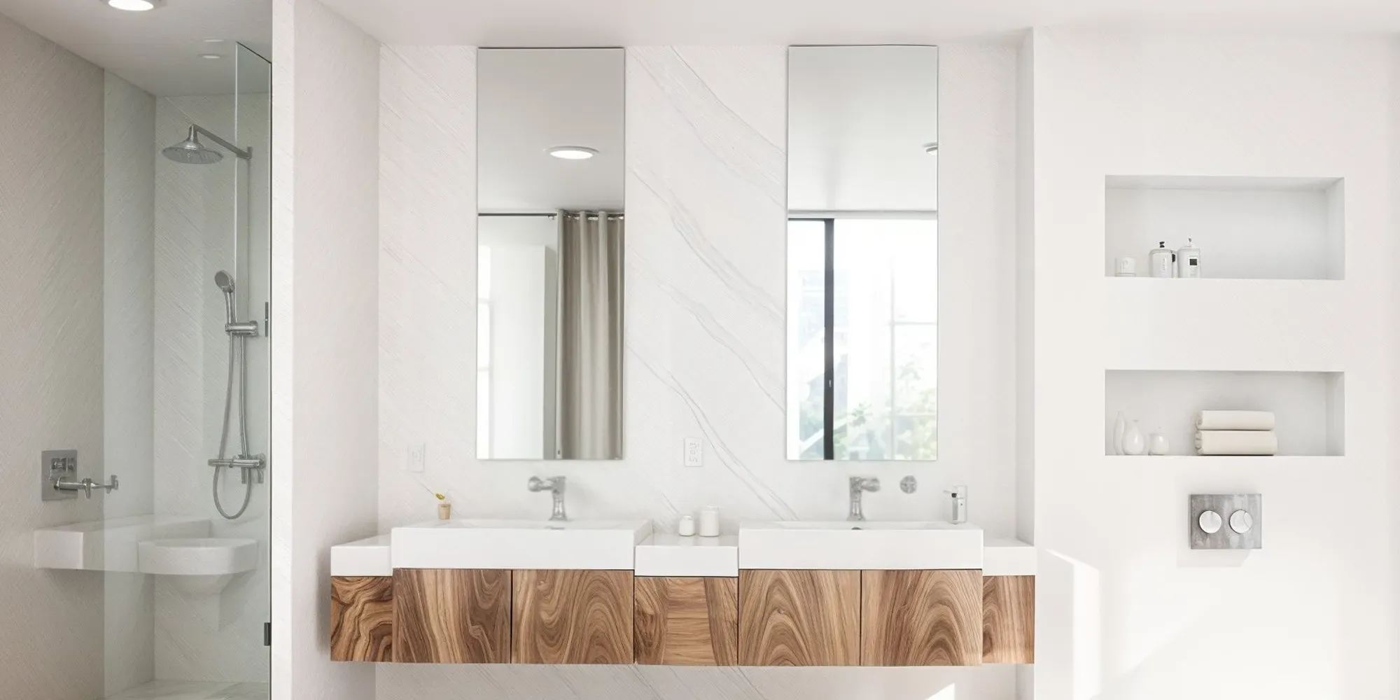 A bright, modern bathroom with a floating wood double vanity, two vertical custom-cut frameless mirrors, and a glass shower.