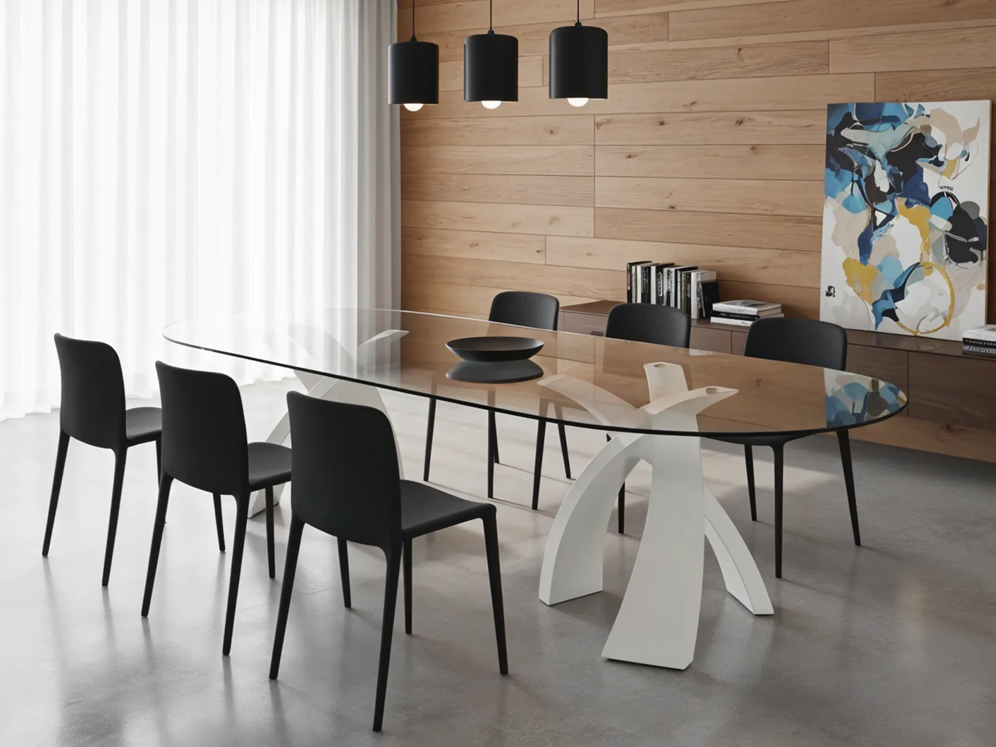 A modern dining room with a long, oval glass-top table on a sculptural white base, surrounded by black chairs against a wood-paneled wall.