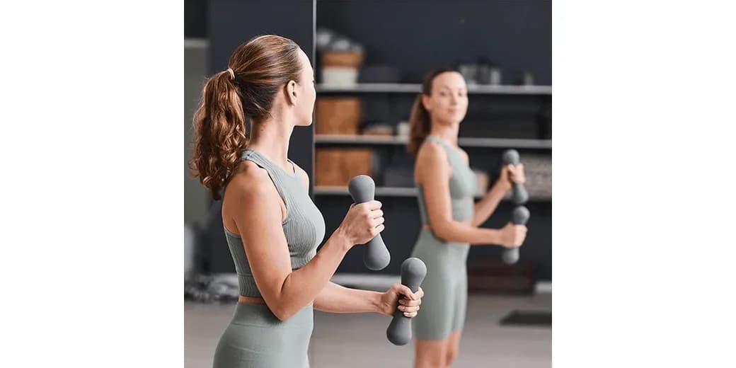 A woman exercising with dumbbells in front of a large, modern mirror, highlighting custom glass solutions including mirrors and tempered glass.