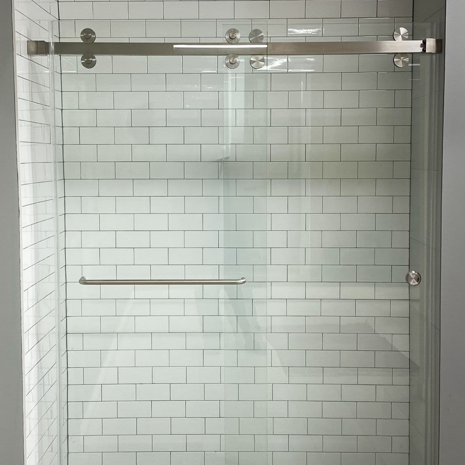 Modern frameless shower doors with a sleek design, featuring tempered glass and a silver sliding rail, complementing a stylish tile backdrop. Perfect for custom glass solutions.