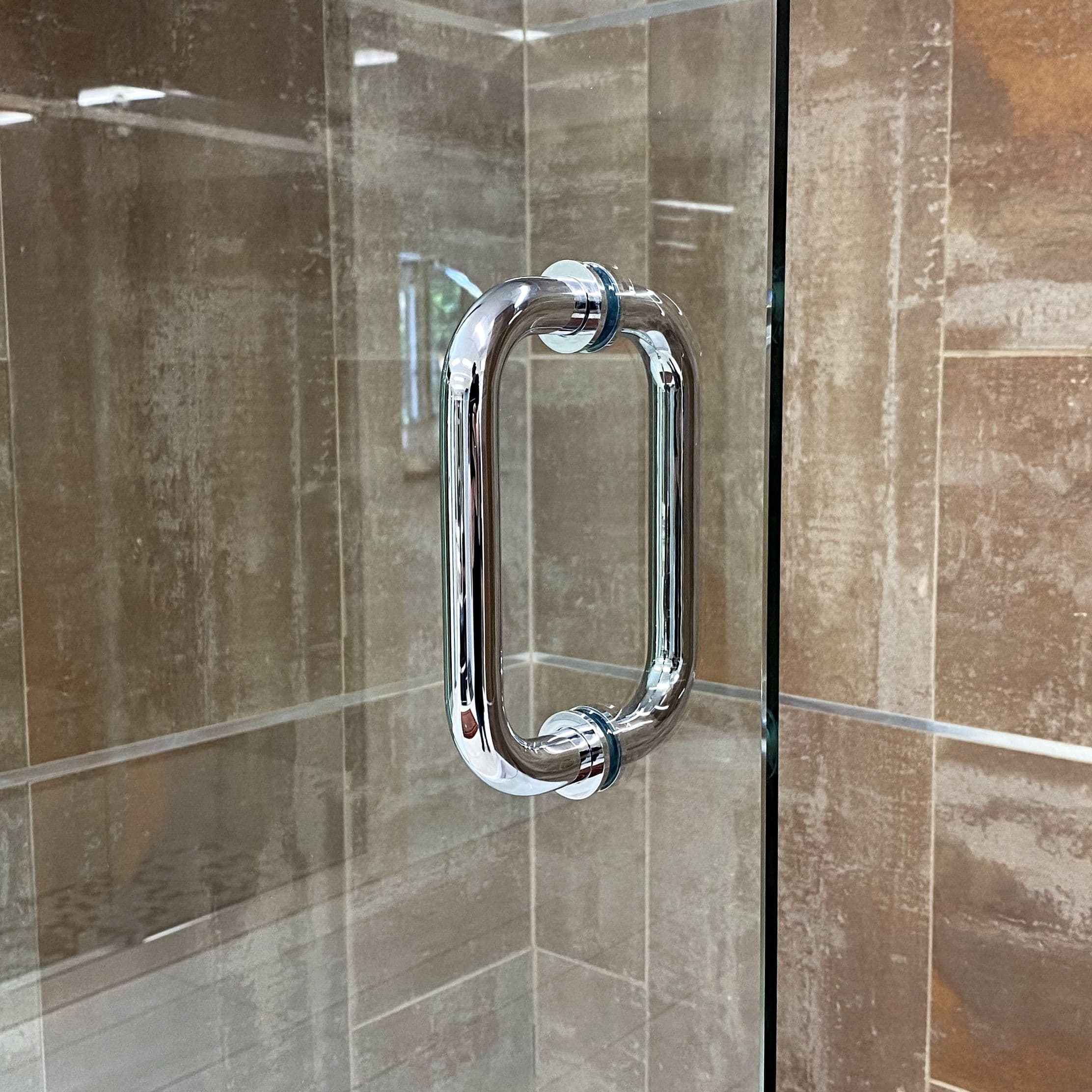 Close-up of a stylish chrome handle on a custom glass shower door, highlighting the sleek design suitable for modern bathrooms featuring tempered glass.