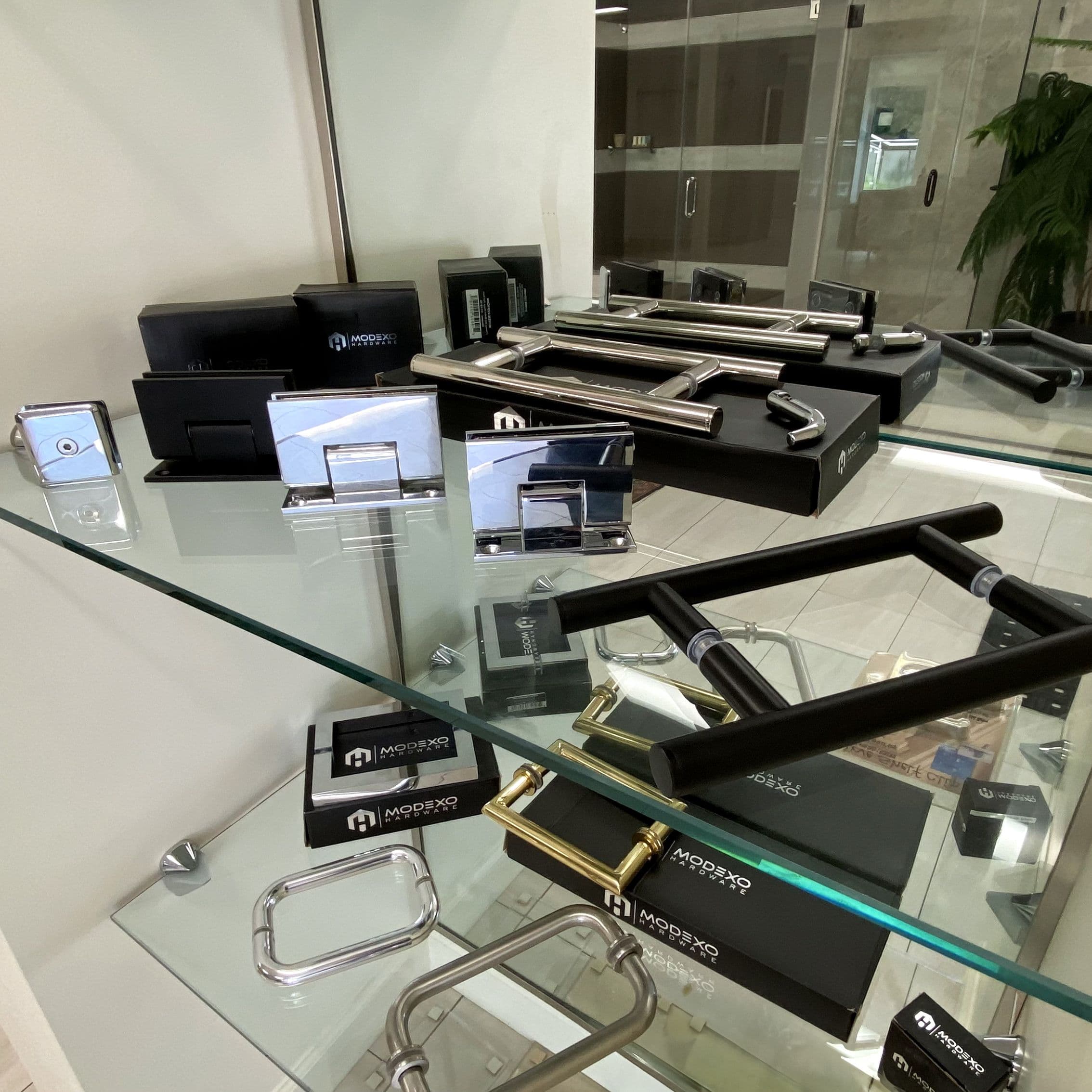 Showroom display featuring custom glass hardware including shower door handles and hinges on tempered glass surfaces, showcasing beveled edges and modern design elements.