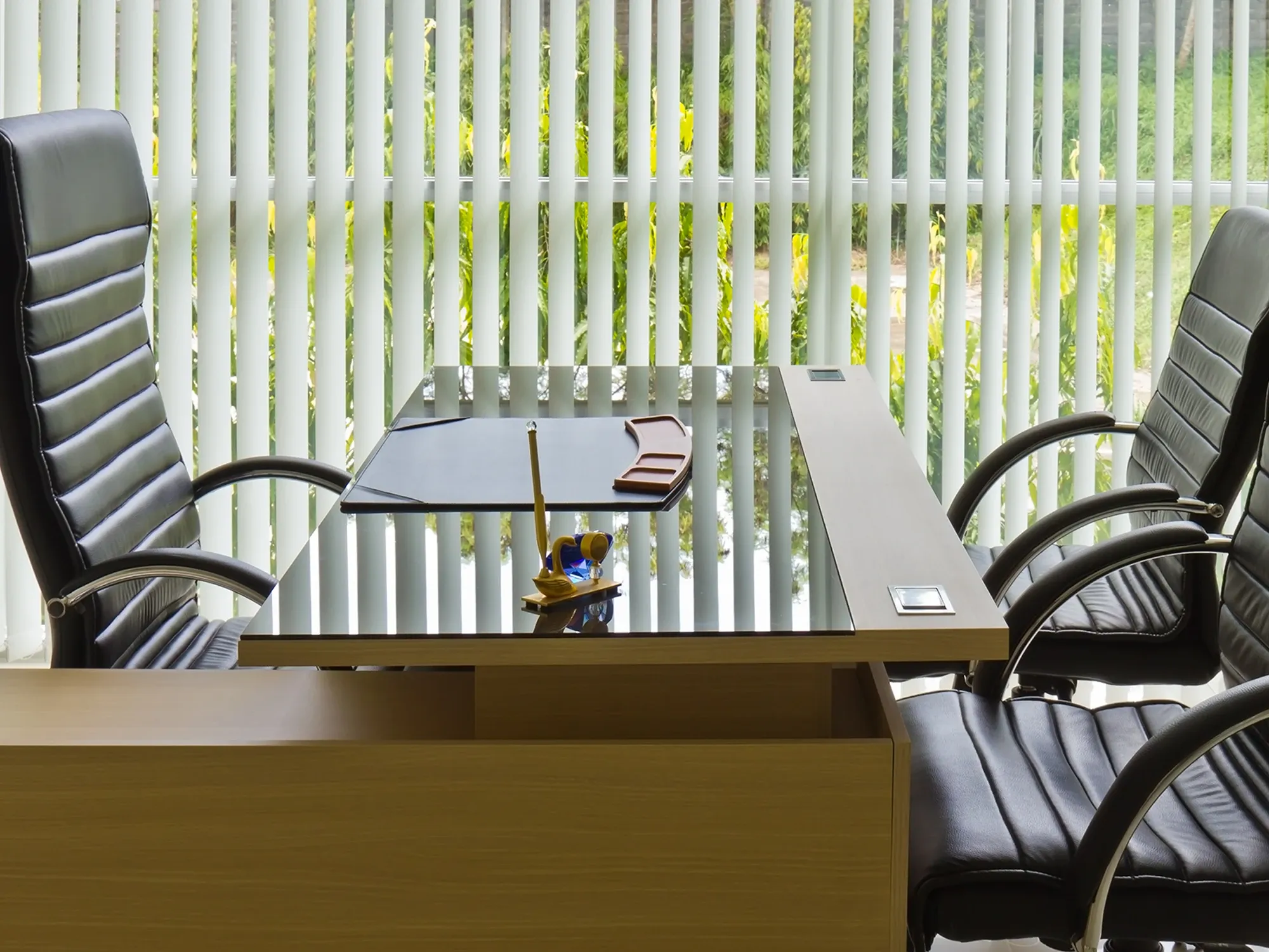 A modern executive office desk with a light wood base, protected by a dark, tinted glass table top cover.
