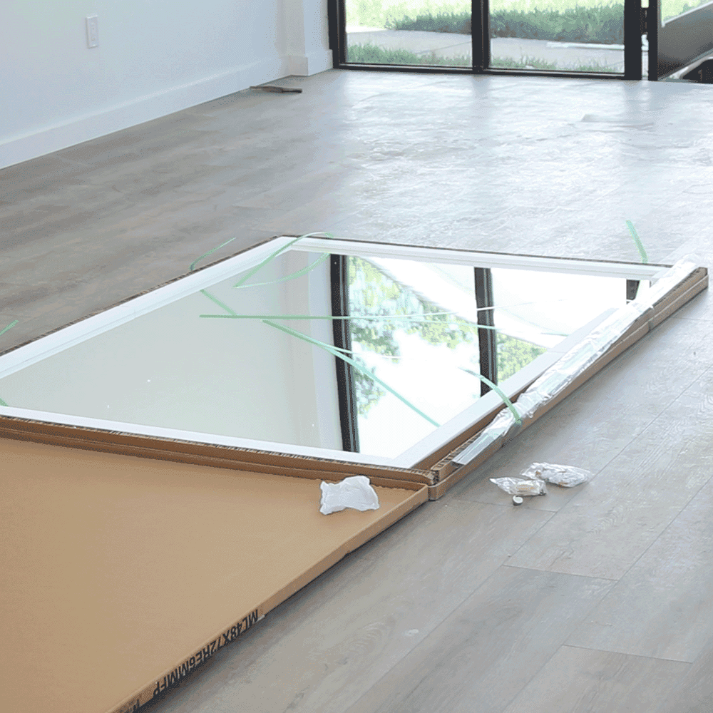 Custom beveled glass mirror resting on packaging in a spacious room, showcasing quality tempered glass options for shower doors and table tops.