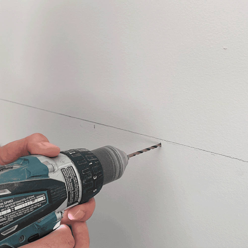 Hand holding a power drill against a wall, preparing to install custom glass shower doors, mirrors, or table tops featuring tempered or beveled glass edges.