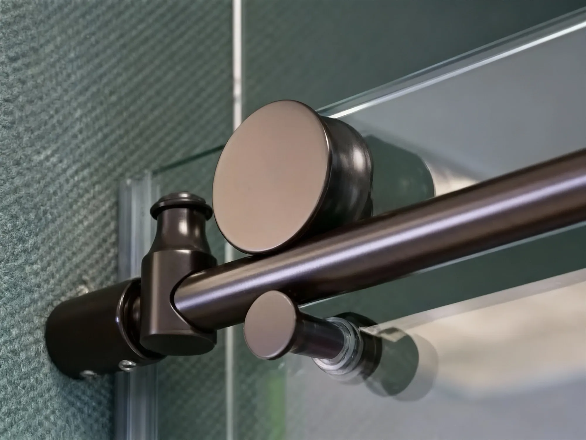 A close-up macro shot of an oil-rubbed bronze sliding shower door roller assembly and track, showing the mechanism on the glass panel.