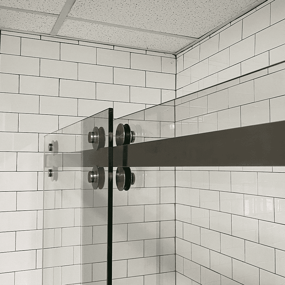 Clear tempered glass shower doors with sleek metal hardware against a white subway tile wall, showcasing custom glass design and beveled edges.