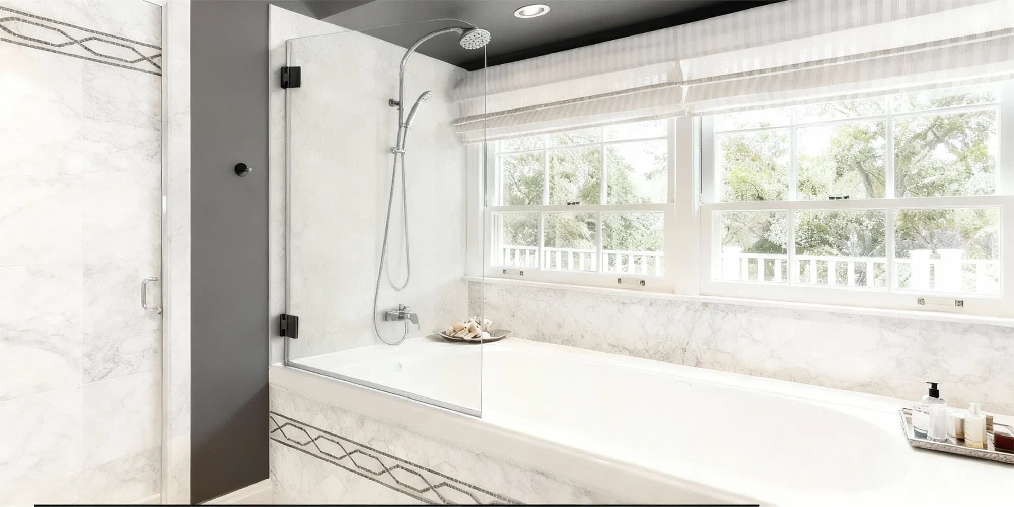 A luxurious marble bathroom featuring a frameless glass tub screen with black hinges, installed on a built-in tub next to large windows.