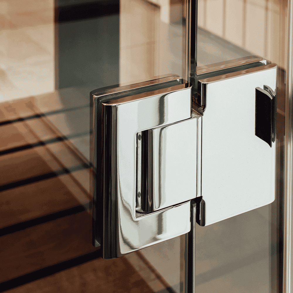 Close-up of a polished chrome hinge on a frameless shower door, showcasing custom glass design with tempered and beveled edges, highlighting quality craftsmanship in shower doors and glass solutions.