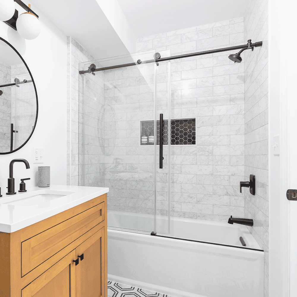 Custom glass shower doors in a modern bathroom with a sleek design, complemented by a round mirror and stylish fixtures. Ideal for showcasing custom solutions for shower doors, tempered glass, and mirrors.