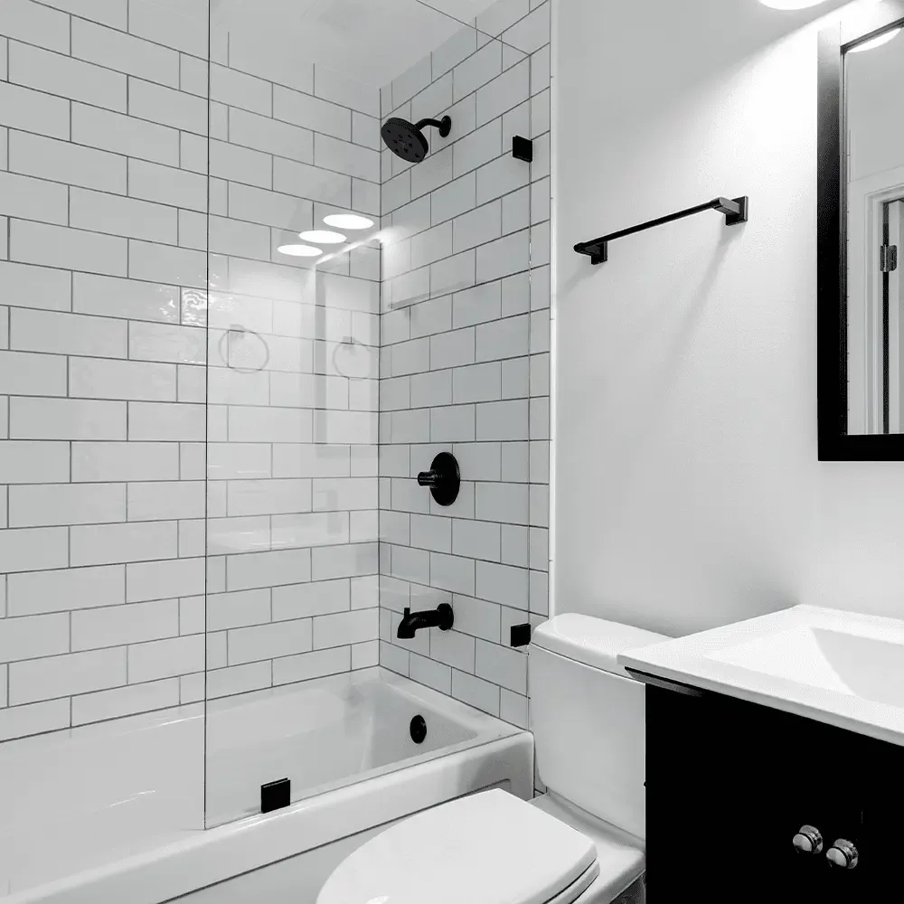 A modern black and white bathroom featuring a tub-shower combo with a frameless glass screen, white subway tile, and bold matte black fixtures.