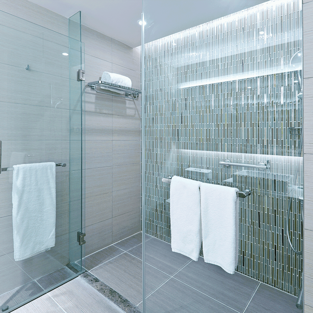 Modern shower design featuring frameless shower doors and custom tempered glass, complemented by stylish tile and illuminated mirror details.