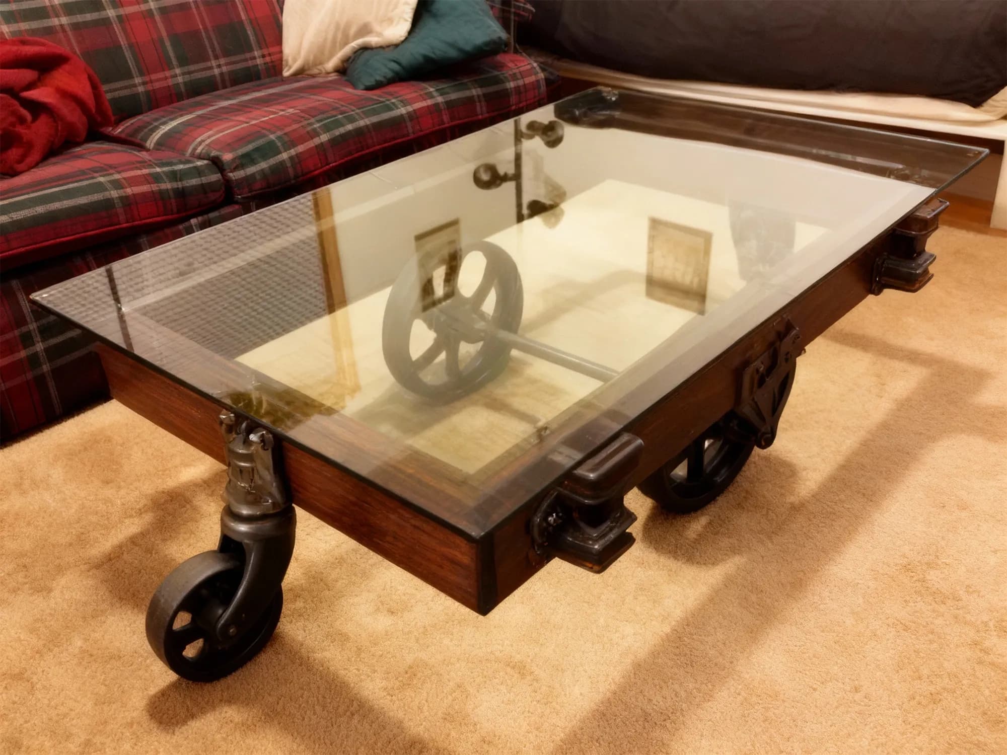 A rustic industrial coffee table made of dark wood and large cast-iron wheels