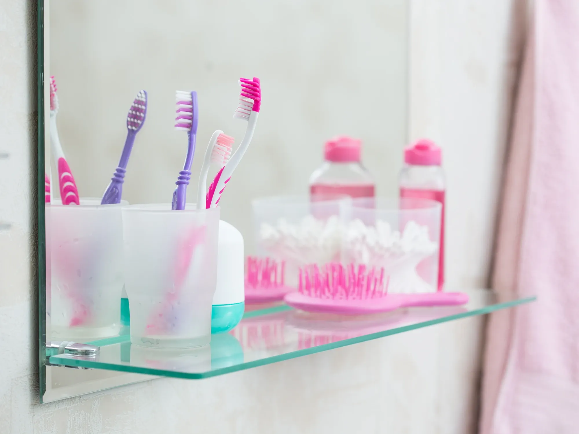 A clear glass bathroom shelf mounted in front of a mirror