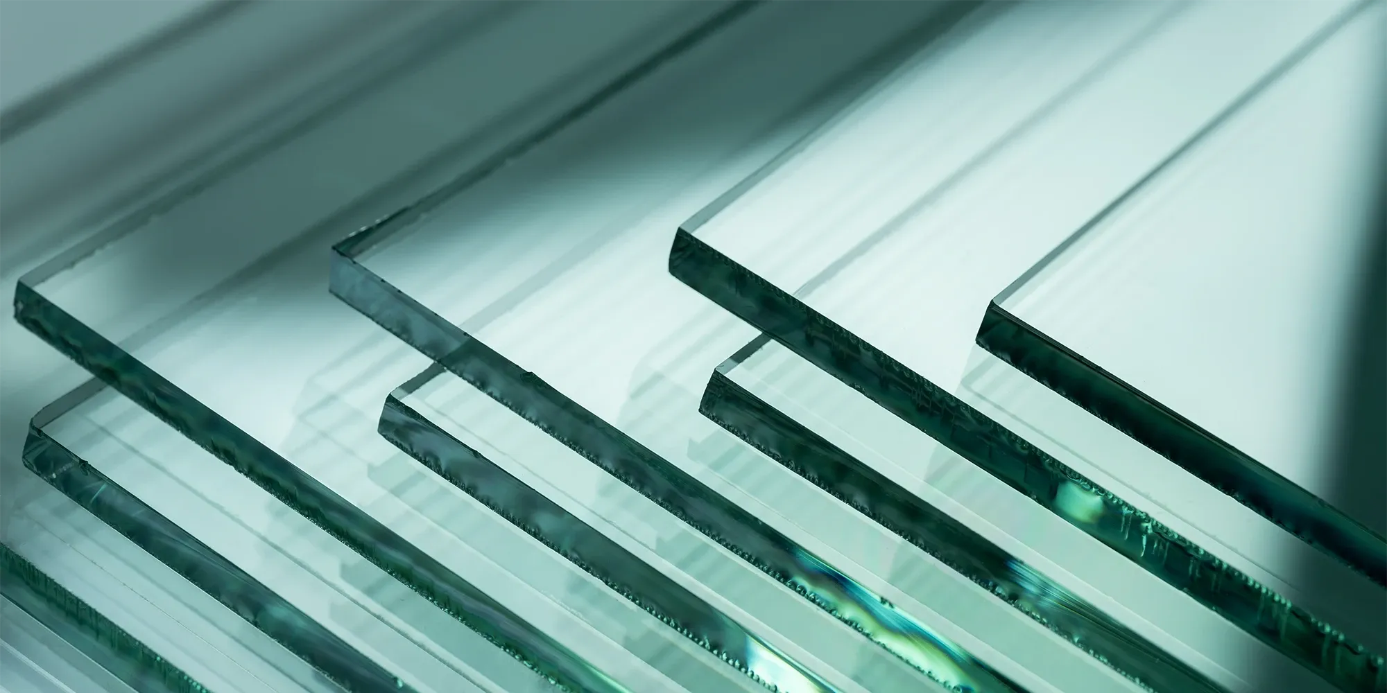 A close-up abstract shot of several overlapping sheets of thick, tempered glass, highlighting their polished edges and clear, greenish tint.