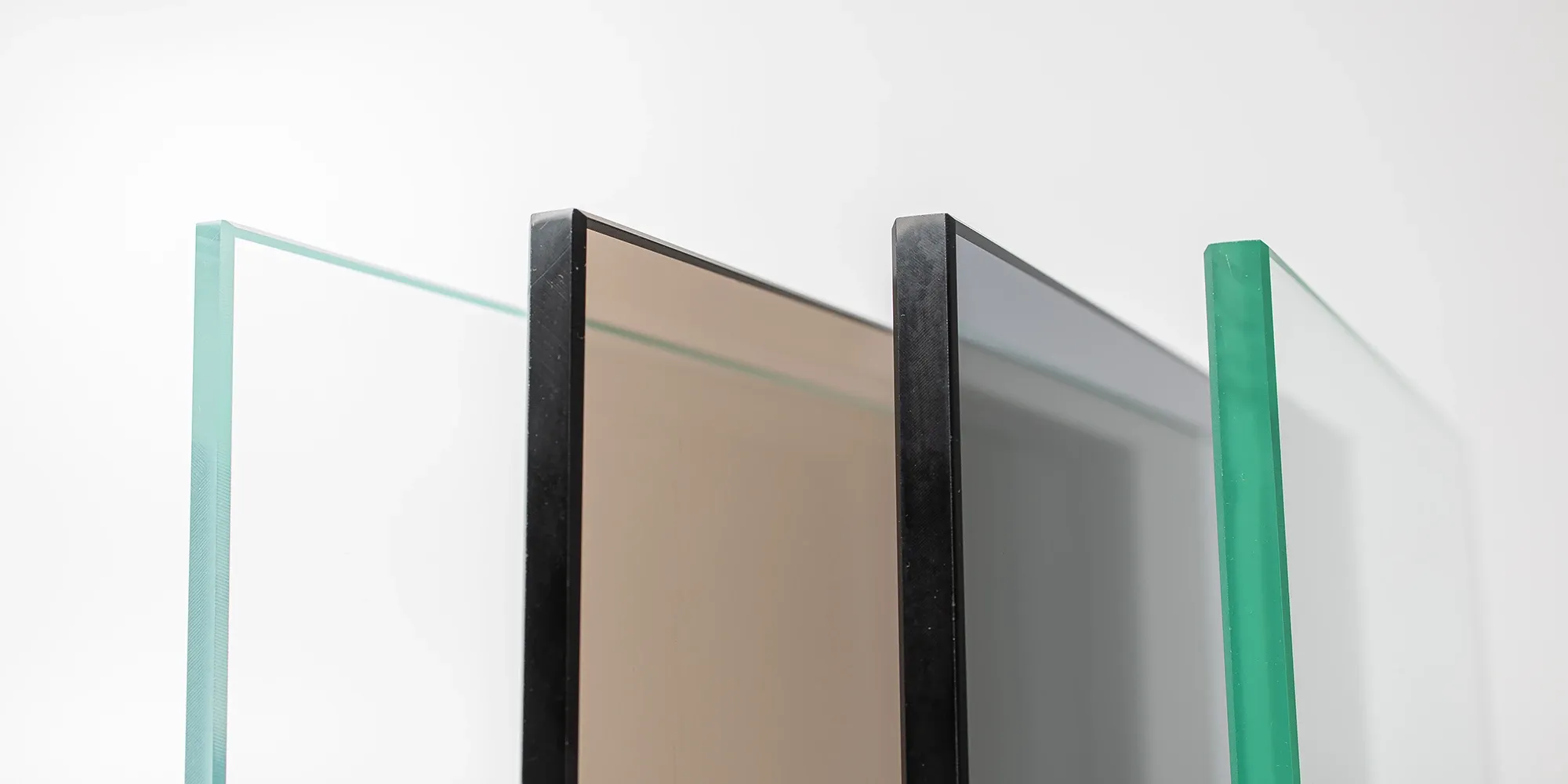 A lineup of different glass panel samples, showcasing various tints such as bronze and grey for custom shower enclosures.