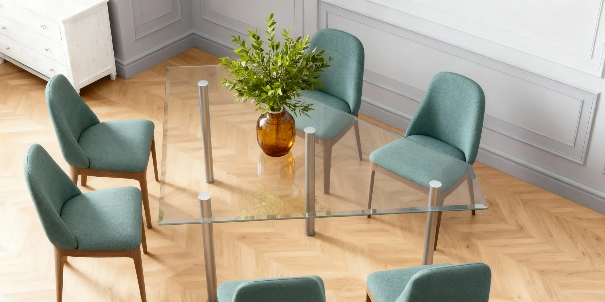 A modern rectangular glass-top dining table with cylindrical chrome legs, surrounded by six teal upholstered chairs on a chevron-patterned wood floor.