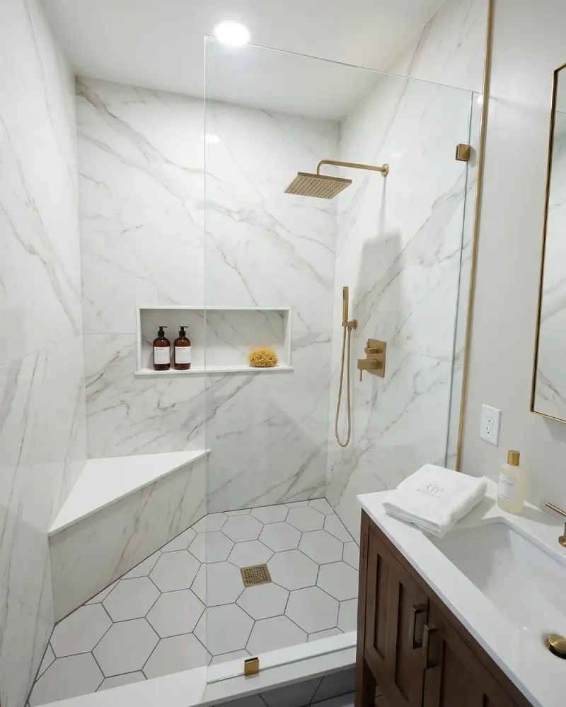Fixed glass shower panel walk-in shower with white marble tile, bench and brass hardware