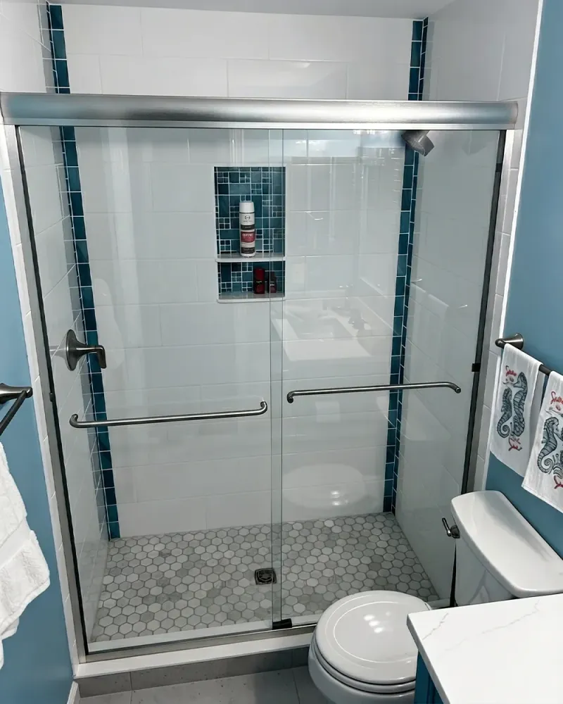 Sliding glass tub door with blue mosaic tile accent and chrome hardware over a bathtub