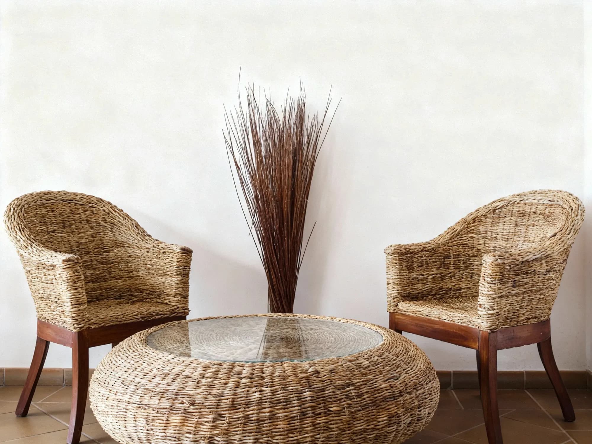 A minimalist patio set with two natural-fiber wicker chairs and a matching round wicker coffee table with a clear glass top.