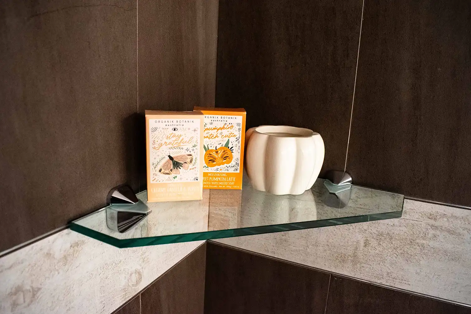 Custom glass shelf displaying skincare products and a decorative vase, featuring tempered glass and beveled glass edge for a sleek, modern look in a shower setting.