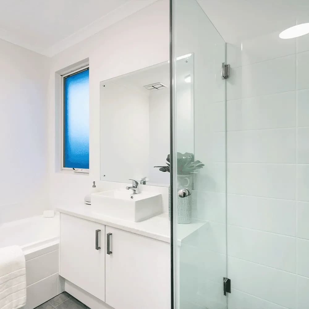 A bright, minimalist all-white bathroom featuring a frameless glass shower screen, a vanity with a vessel sink, and a bathtub.