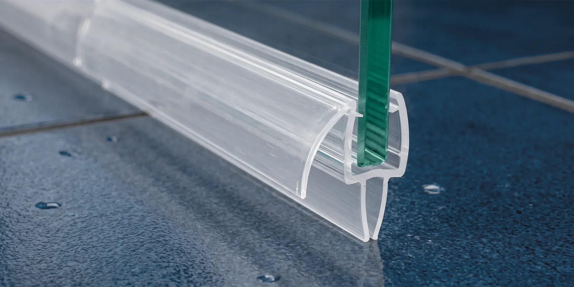 Close-up of a clear shower door bottom sweep seal fitted to the edge of a glass door
