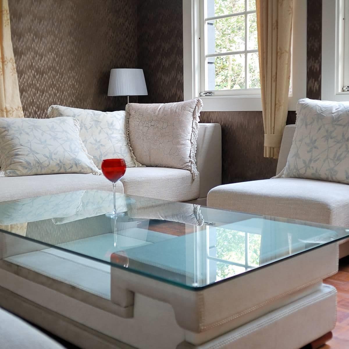 Modern living room with glass coffee table, beige sofas, and red wine glass