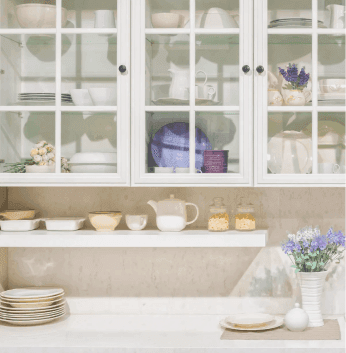 Elegant kitchen display featuring glass cabinets, showcasing table tops and kitchenware, complemented by decorative elements like flowers, ideal for custom glass solutions including tempered and beveled glass edges.