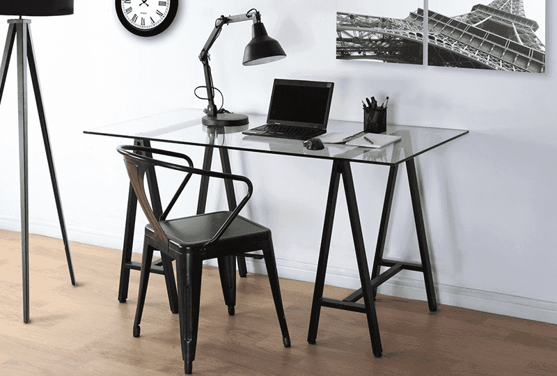 Clear tempered glass table top in a modern workspace setting with a black chair, laptop, and desk lamp, showcasing custom glass design and functionality.