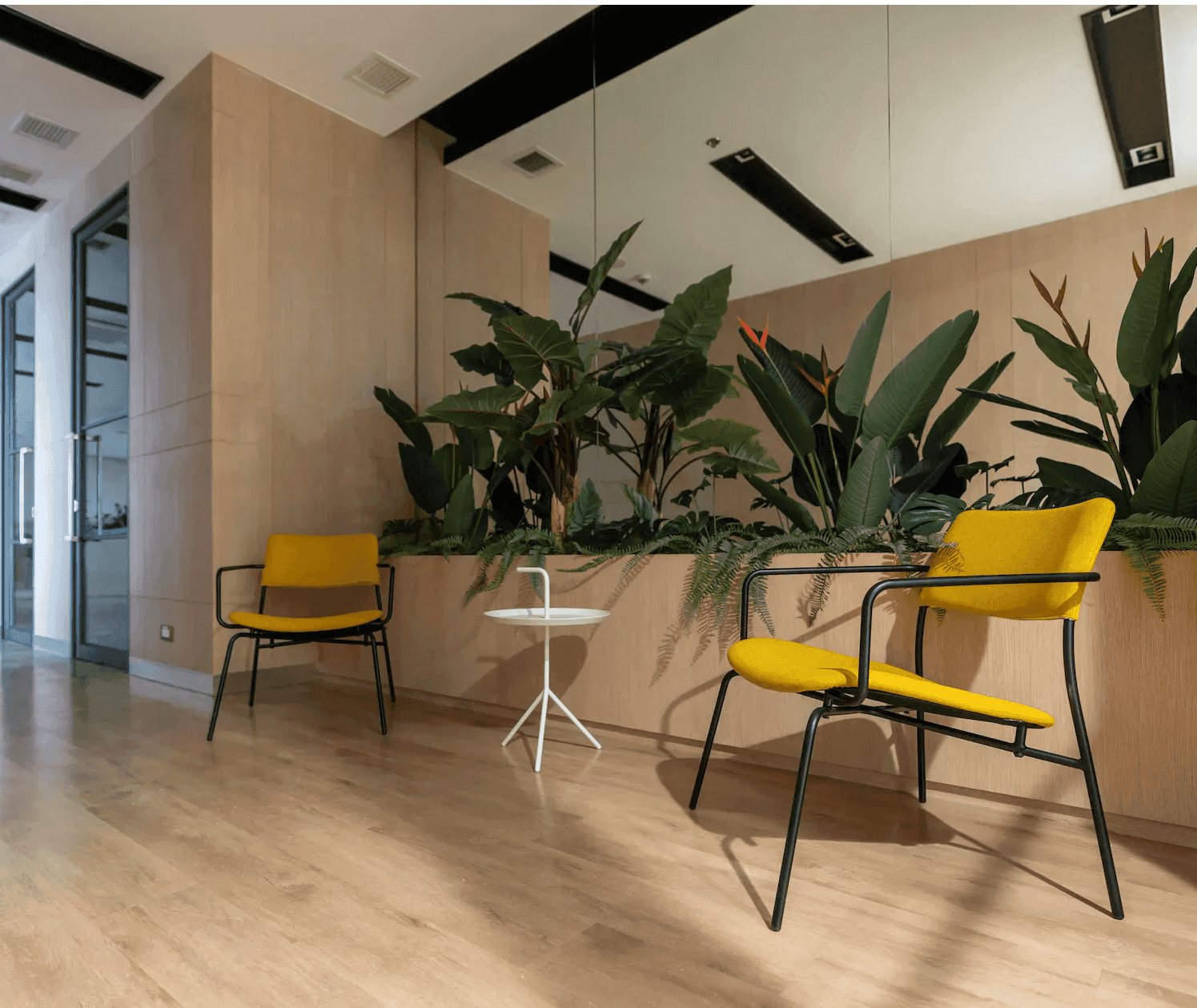 Modern interior featuring custom glass mirrors, a minimalist table, and vibrant yellow chairs amidst lush greenery, reflecting a chic design aesthetic ideal for showcasing shower doors, table tops, and tempered glass solutions.