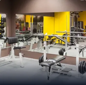 Custom mirrors reflecting fitness equipment in a modern gym with various weights and benches, showcasing versatile applications of tempered glass and mirrors.
