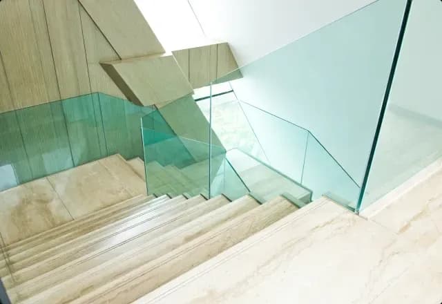 Custom glass railing in a modern staircase, featuring tempered glass panels and sleek design, ideal for enhancing interiors with shower doors, mirrors, and table tops.