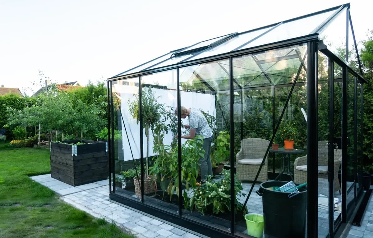 A glass greenhouse with a gardener tending to plants, showcasing custom glass panels ideal for shower doors, table tops, and mirrors, complemented by tempered and beveled glass edges.