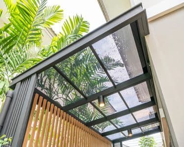 Custom glass canopy with tempered glass, showcasing a modern design and surrounded by lush greenery, perfect for enhancing outdoor spaces.