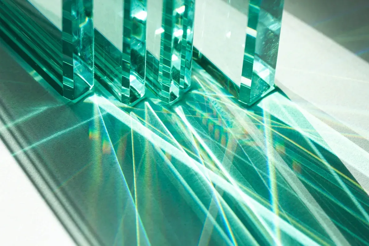 Tempered glass pieces creating stunning light reflections, showcasing custom glass solutions for shower doors, table tops, mirrors, and beveled glass edges.