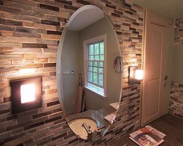 Oval mirror with beveled edges mounted on textured stone wall, showcasing custom glass design in a stylish bathroom setting, highlighting shower doors and tempered glass features.