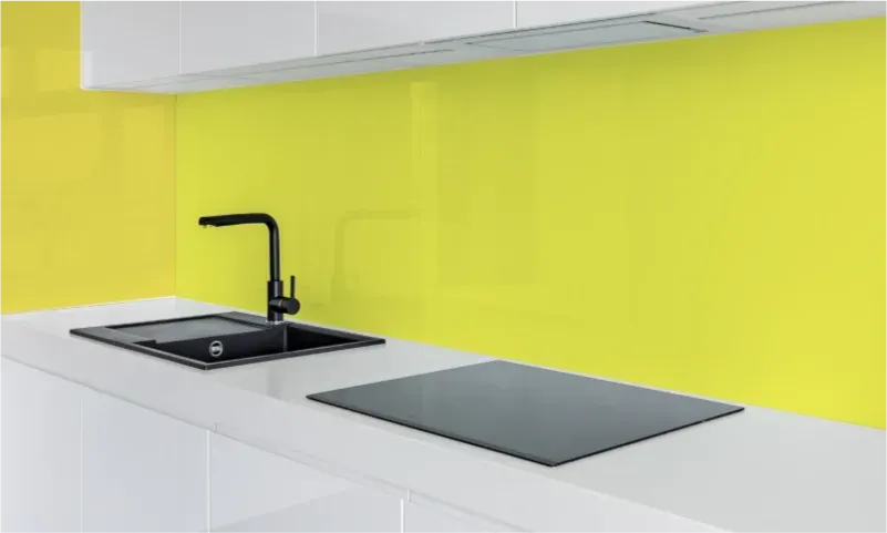 Modern kitchen featuring a sleek black countertop with an integrated sink and colorful yellow glass backsplash, highlighting custom glass applications for countertops and interior design.