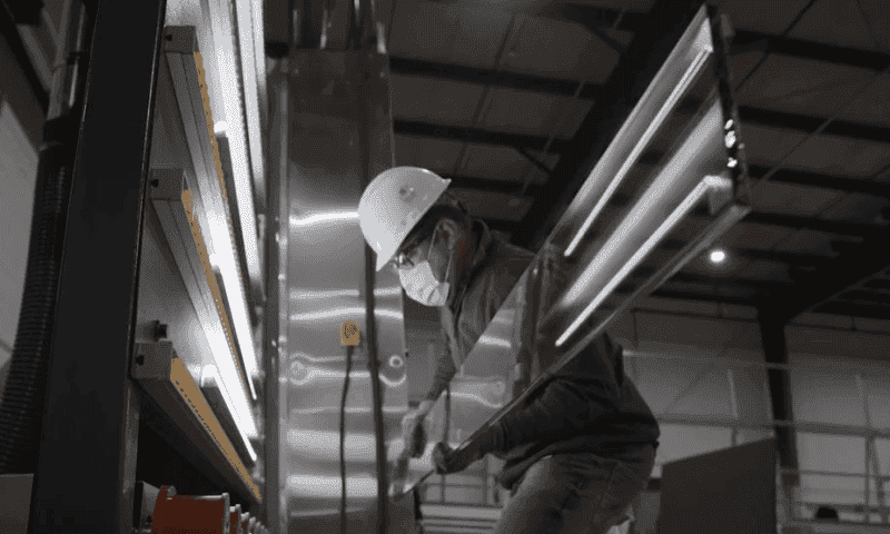 Worker handling custom tempered glass for shower doors and table tops in a manufacturing facility, showcasing precision craftsmanship and safety measures.
