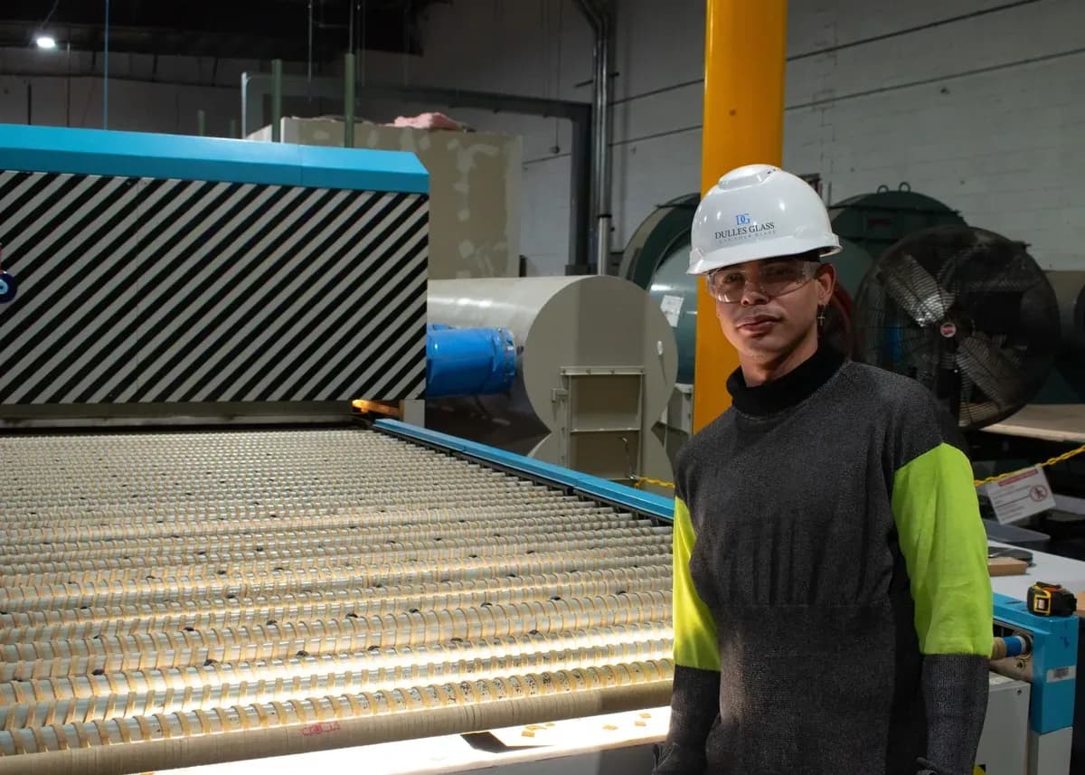 Worker in a glass manufacturing facility next to advanced machinery, focusing on custom glass products including shower doors, table tops, and mirrors with tempered and beveled glass edges.
