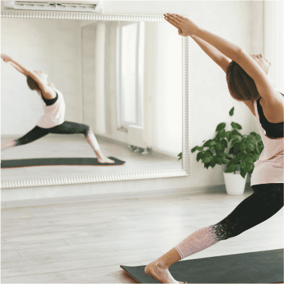 A woman gracefully practicing yoga in front of a gym mirror, focusing on her form and inner peace.
