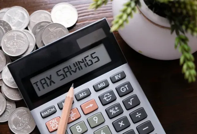 Calculator displaying TAX SAVINGS next to coins and a plant, symbolizing financial planning and potential budget for custom glass solutions like shower doors, table tops, mirrors, tempered glass, and beveled glass edges.