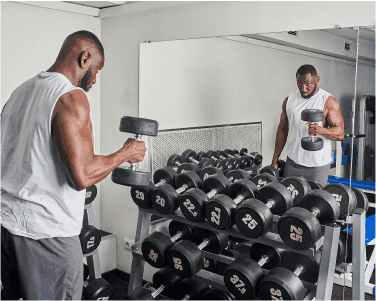Man lifting weights in a gym with a mirrored wall, showcasing custom glass mirrors, emphasizing fitness and strength training.