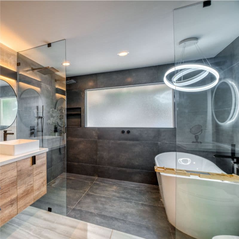 Modern bathroom featuring custom glass shower doors, a sleek tub, tempered glass accents, and a beveled mirror, showcasing a contemporary design.